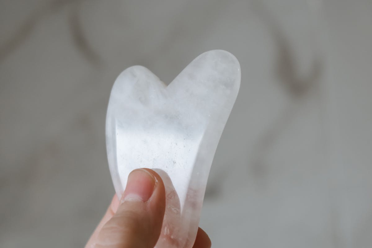 Main tenant un outil de gua sha en quartz translucide devant un fond clair