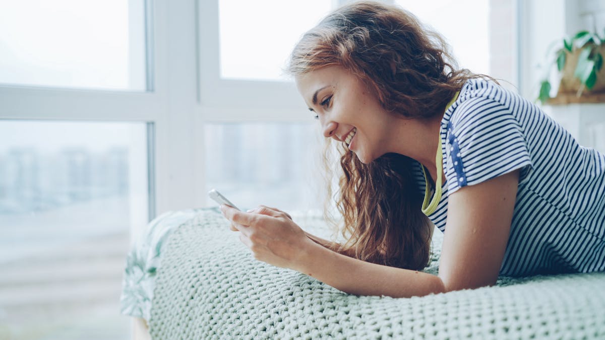Femme souriante en train d'écrire un message sur son téléphone