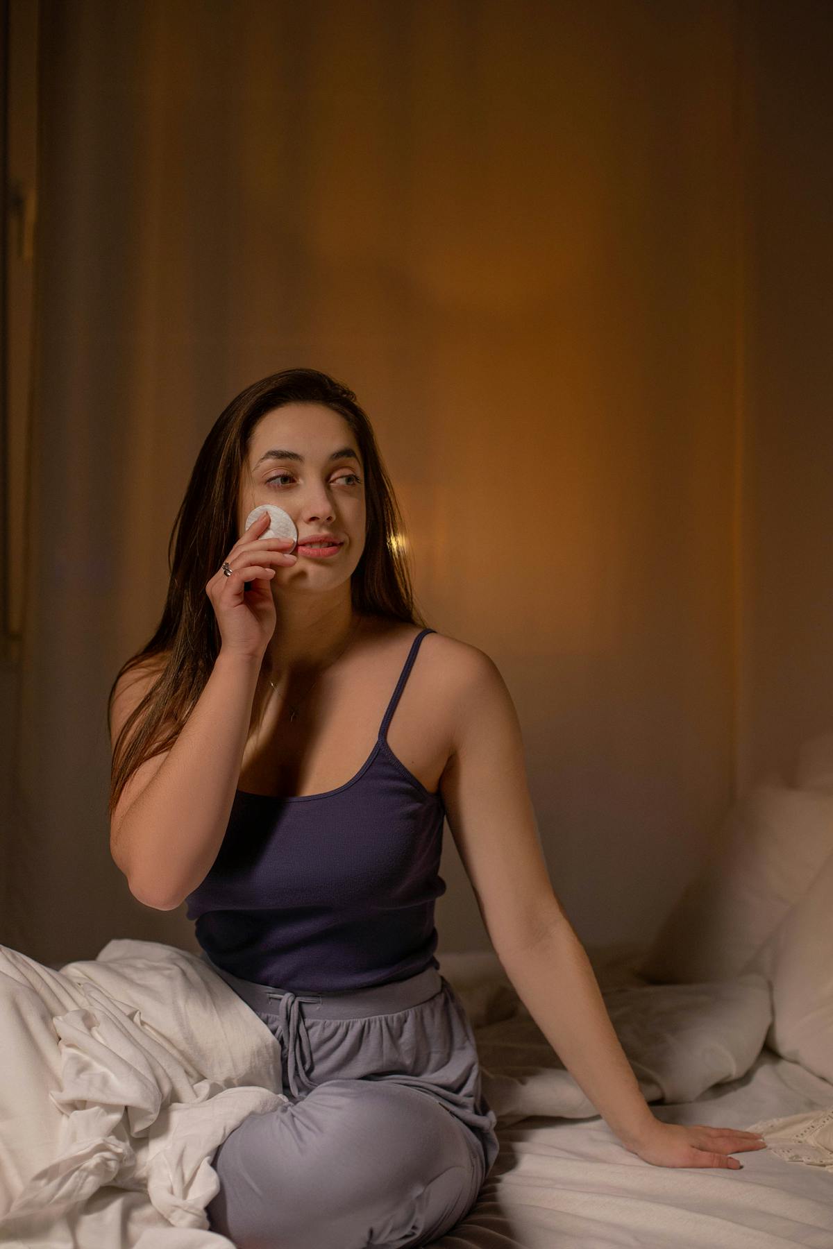 Femme appliquant un disque de coton démaquillant dans une ambiance chambre apaisante