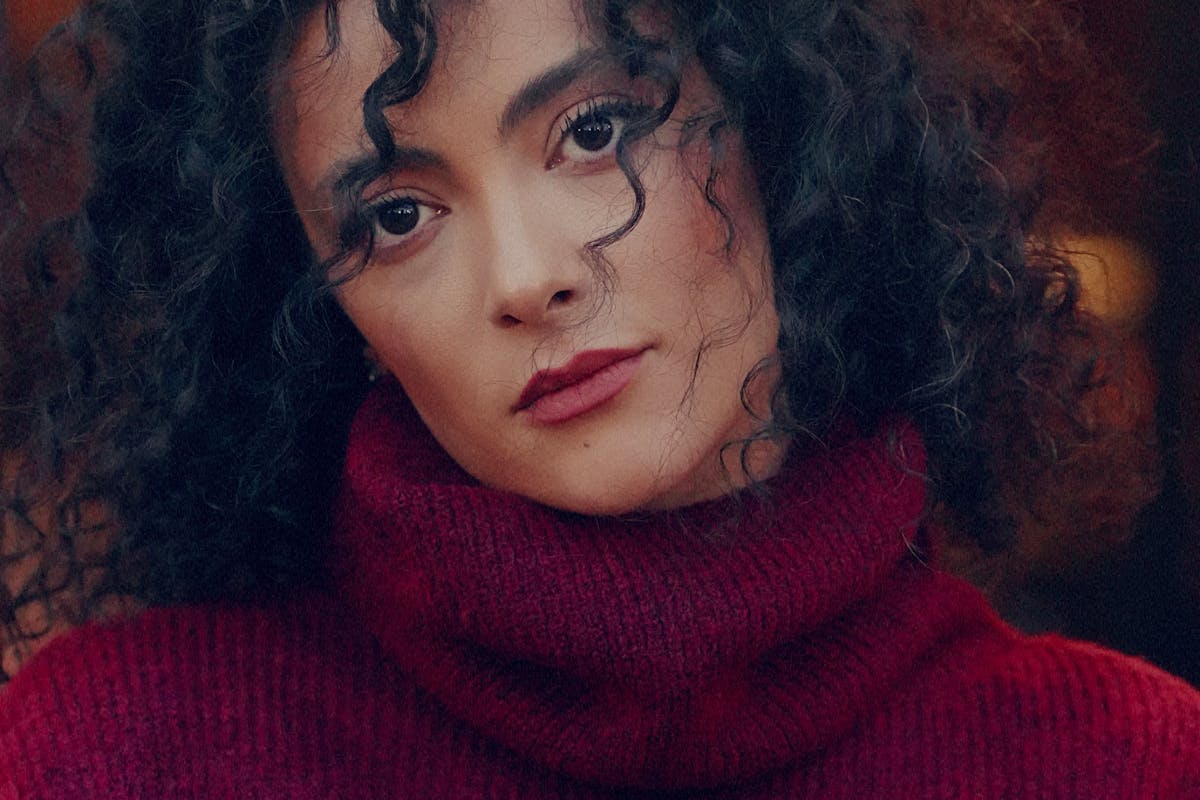 Femme aux cheveux bouclés bruns et définis souriant en lumière naturelle